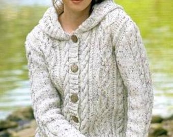 May include: A woman wearing a white hooded cable-knit cardigan with wooden buttons. The sweater has a speckled pattern and long sleeves. The woman is sitting outdoors.