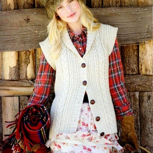 May include: A woman wearing a cream-colored cable-knit vest with brown buttons over a red plaid shirt and a floral skirt. She is also wearing a fur hat and holding a rolled-up red blanket. The overall style is rustic and outdoorsy.