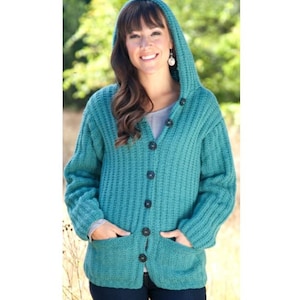 Può includere: Cardigan con cappuccio color teal, con bottoni neri e due tasche anteriori. Il maglione è realizzato in un tessuto a maglia spesso e strutturato. Il cappuccio è alzato e il cardigan è abbottonato sul davanti.