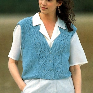 May include: A light blue knitted vest with a cable knit design and button closure. The vest is worn over a white collared shirt and light-colored pants. The vest features a textured pattern and a V-neck.