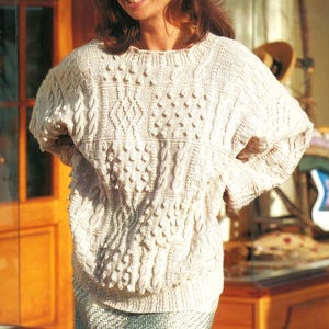May include: Cream-colored, textured knit sweater with a crew neck and intricate cable and bobble stitch patterns. The sweater has a relaxed fit and long sleeves, perfect for cooler weather. The design features a combination of textures and patterns.