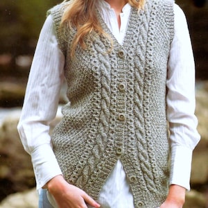 May include: A gray knitted vest with a cable knit design and button closure. The vest is worn over a white button-down shirt. The vest has a V-neck and is made of a soft, textured yarn.