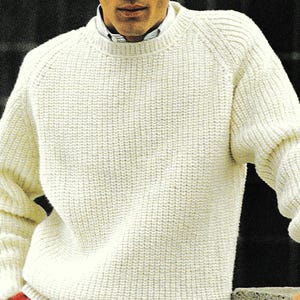 Könnte beinhalten: Ein weißer Strickpullover mit Rundhalsausschnitt. Der Pullover hat eine gerippte Struktur und wird über einem roten Hemd getragen.