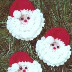 May include: Three white crocheted Santa Claus ornaments with red hats and white pom-poms. The ornaments have black eyes and red noses.