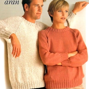 Puede incluir: Dos personas con jerséis de punto. Uno es de color beige claro, el otro coral. Ambos tienen dobladillos y puños acanalados. La palabra "aran" está en la esquina superior izquierda. Adecuado para el otoño.