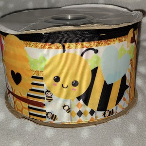 May include: A roll of yellow, black, and white ribbon with a bee and honeycomb pattern. The ribbon has a cute cartoon bee with a heart and a honeycomb design.