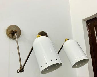 May include: Two white metal wall sconces with brass accents and adjustable arms. The sconces have a white finish and a perforated design.