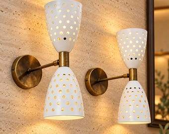 May include: Two wall-mounted light fixtures featuring dual white conical shades with perforated circular patterns. Each lamp has a brass-toned metal arm and a circular wall plate, with light emitting through the holes in the shades.