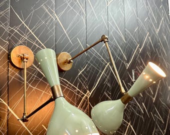 May include: Two wall-mounted light fixtures with adjustable arms. The fixtures have a brass finish and green metal shades with a perforated pattern. The lights are turned on and illuminating the room.