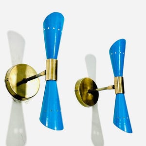 Puede incluir: Un par de apliques de pared de latón vintage con pantallas de esmalte azul. Las pantallas tienen un diseño único y curvo y están acentuadas con pequeños puntos blancos.