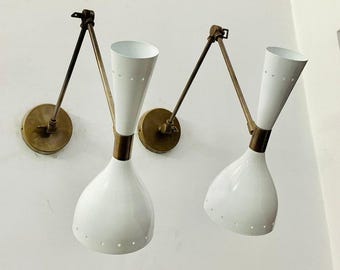 May include: Two white and brass wall sconces with adjustable arms. The sconces have a modern design and are perfect for adding a touch of style to any room.