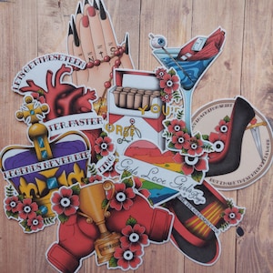 May include: A collection of colorful tattoo-style stickers. Designs include a heart, crown, boxing gloves, high heel, martini glass, and a pack of cigarettes. Text includes "Legends Never Die", "Girls Love Girls Boys", and "Victorious".