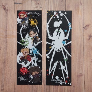 May include: Two black and white bookmarks with a white spider design and colourful paint splatters. The bookmark on the left features four cartoon characters and the text "What the hey, can we try?" and "So long and goodnight". The bookmark on the right has the text "Bee Dim Boutique".