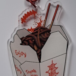May include: Clear acrylic keychain featuring a Chinese takeout box filled with noodles and chopsticks. The keychain has a red bat-shaped clasp and includes the text "Enjoy", "Thank You", and "One of Us".