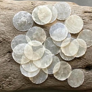 May include: A collection of translucent, circular capiz shell discs with a natural, pearlescent finish. These thin, flat, and round pieces are arranged in a cluster, showcasing their semi-transparent quality and smooth, slightly irregular edges.
