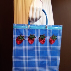 May include: A blue and white plaid tote bag with a blue handle and four red strawberry appliques.