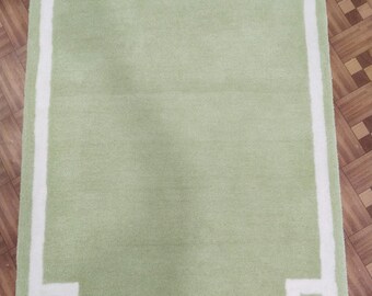 Puede incluir: Una alfombra verde claro con un borde blanco. El borde tiene un diseño geométrico.