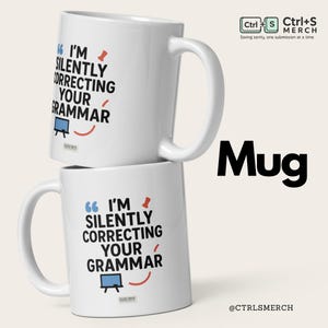 Peut inclure: Deux mugs en céramique blanche empilés. Chaque mug a une anse noire et affiche le texte "I'M SILENTLY CORRECTING YOUR GRAMMAR" en bleu et noir, avec un tableau blanc et un point d'exclamation rouge. Le mot "Mug" est en noir.