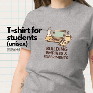 May include: Gray unisex t-shirt with the text "T-shirt for students" and a graphic of a laptop, beaker, coffee cup, and notepad. The phrase "BUILDING EMPIRES & EXPERIMENTS" is below the graphic.