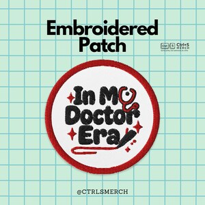 以下が含まれることがあります： 赤い縁と白い中心部を持つ刺繍パッチ。「In My Doctor Era」のテキストが黒と赤で、聴診器のグラフィックが描かれています。「Embroidered Patch」の文字が上部にあります。