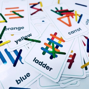 May include: A set of colorful wooden sticks arranged to form different shapes and words on white cards. The cards include the words "orange", "yellow", "blue", "ladder", "carrot", and "use".