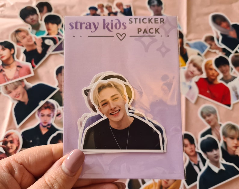 May include: A purple and white sticker pack with the text "stray kids sticker pack" and a heart. The pack features a sticker of a young man with blonde hair and a black shirt.