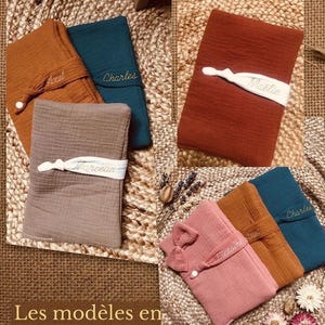 Puede incluir: Art&iacute;culos de tela doblados en varios colores, incluyendo &oacute;xido, verde azulado y rosa, se exhiben sobre una superficie tejida. Cada art&iacute;culo est&aacute; asegurado con una banda blanca, algunos bordados con nombres. El texto "Les mod&egrave;les en double gaze de coton unis" es visible.