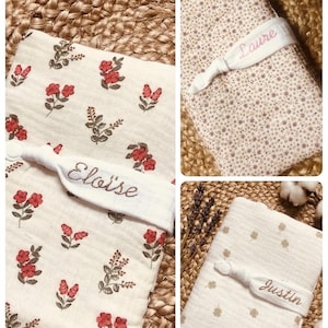 Puede incluir: Una colecci&oacute;n de mantas personalizadas para beb&eacute;s. Una manta presenta un estampado floral con flores rojas, otra tiene un peque&ntilde;o patr&oacute;n de estrellas y la tercera tiene un patr&oacute;n de tr&eacute;boles. Cada manta est&aacute; asegurada con una banda blanca bordada con un nombre.