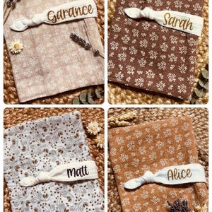 Puede incluir: Cuatro mantas de beb&eacute; personalizadas con estampados florales en varios colores: beige, marr&oacute;n, azul claro y naranja. Cada manta tiene una banda el&aacute;stica blanca con un nombre bordado en dorado: Garance, Sarah, Matt y Alice. Flores secas y espigas de trigo dispuestas alrededor.