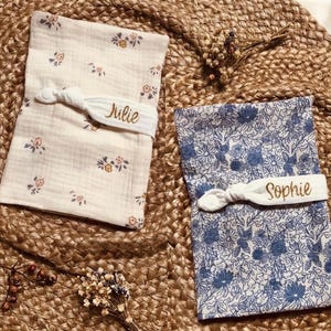 Puede incluir: Dos baberos de tela para beb&eacute;, uno crema con estampado floral y otro azul con un estampado floral. Cada babero se asegura con una banda el&aacute;stica blanca bordada con un nombre, "Julie" y "Sophie".