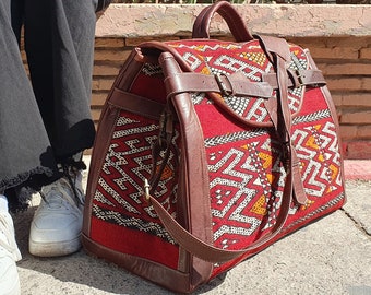 May include: A large, red and brown leather travel bag with a geometric pattern. The bag has a long strap and a buckle closure.