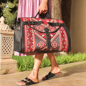 May include: A black leather travel bag with a red, white and black patterned fabric design. The bag has two straps and a top handle.