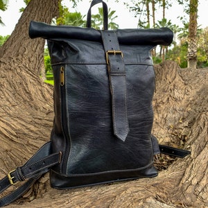 May include: A black leather backpack with a roll-top closure and a buckle strap. The backpack has a zippered pocket on the front and a strap on the side.