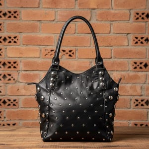 May include: Black leather handbag with silver-colored studs. The bag has a curved top, two handles, and a zipper closure. The studs are evenly spaced across the front and sides of the bag.