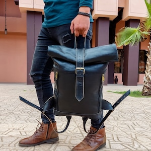 Pode incluir: Uma mochila de couro preto com fecho de rolo e alças ajustáveis. A mochila tem um fecho de fivela e ferragens douradas.
