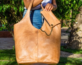 May include: A large, light brown leather tote bag with a smaller, matching leather pouch attached. The tote bag has a long strap and a chain detail.