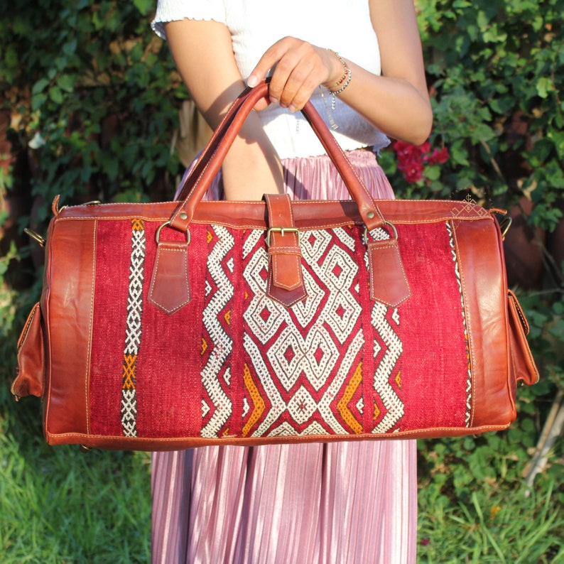 May include: A red and brown leather travel bag with a geometric pattern. The bag has a top handle and a shoulder strap.