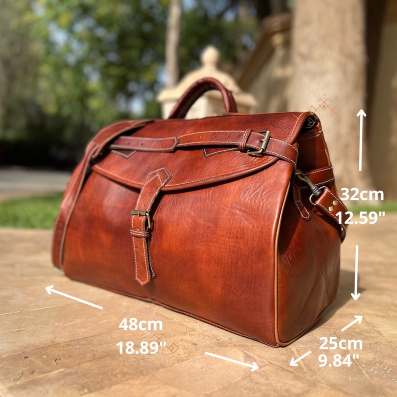 May include: A brown leather duffel bag with a top handle, a shoulder strap, and buckle closures. The bag measures 18.89 inches in length, 9.84 inches in width, and 12.59 inches in height, featuring visible stitching and metallic hardware accents.