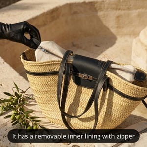 May include: A woven straw tote bag with black leather detailing. The bag has a black leather flap with a silver clasp and long black leather straps. It has a removable inner lining with a zip. A gloved hand is unzipping the inner lining.
