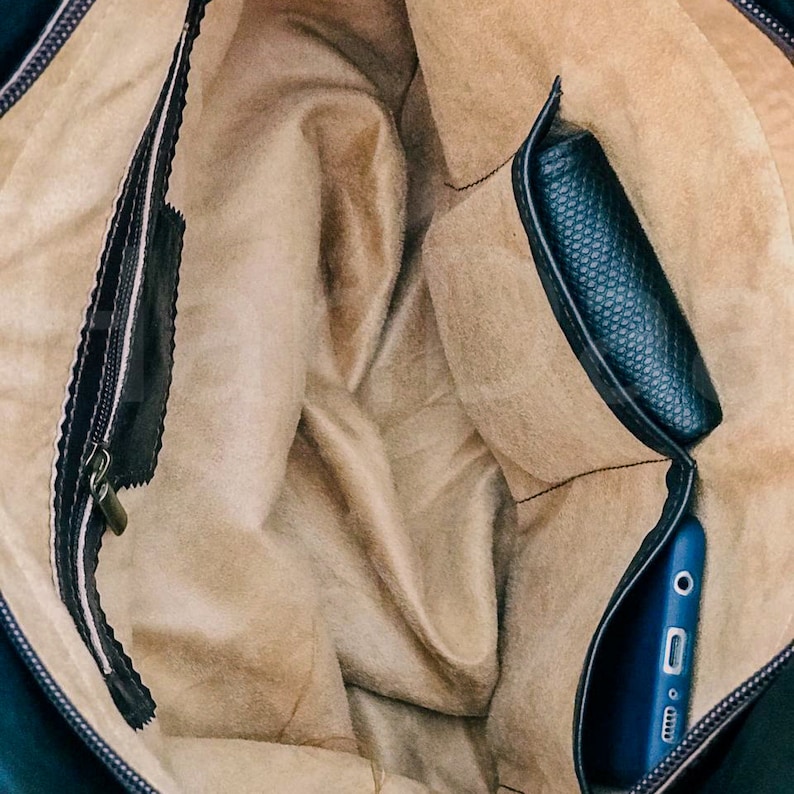 May include: The inside of a black leather bag with a beige lining. The bag has a zipper closure and a small pocket on the side. A blue phone is in the pocket.
