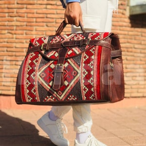 May include: A brown leather travel bag with a red, white and black patterned fabric front. The bag has a large main compartment and a smaller front pocket.