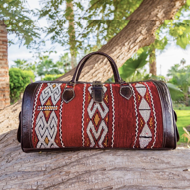May include: A red, white, and brown leather and fabric travel bag with a geometric pattern. The bag has a top handle and a zipper closure.
