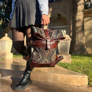 May include: A brown leather backpack with a flap closure and a patterned fabric lining. The backpack has a buckle closure and a strap.