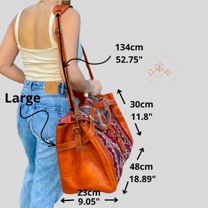 May include: A large, brown leather tote bag with a colourful woven fabric panel. The bag has a long adjustable strap and measures 48cm tall, 30cm wide, and 23cm deep.