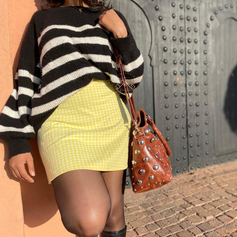 May include: A woman wearing a black and white striped sweater with a yellow gingham skirt and a brown studded handbag.