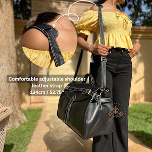 May include: A black leather bag with a top handle and an adjustable shoulder strap measuring 52.75 inches. The bag features a flap closure with a buckle, visible white stitching, and gold-toned metal hardware. A circular inset shows the strap.