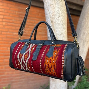 May include: A black leather duffel bag with a red, orange, and white woven pattern. The bag has a top handle and a shoulder strap.