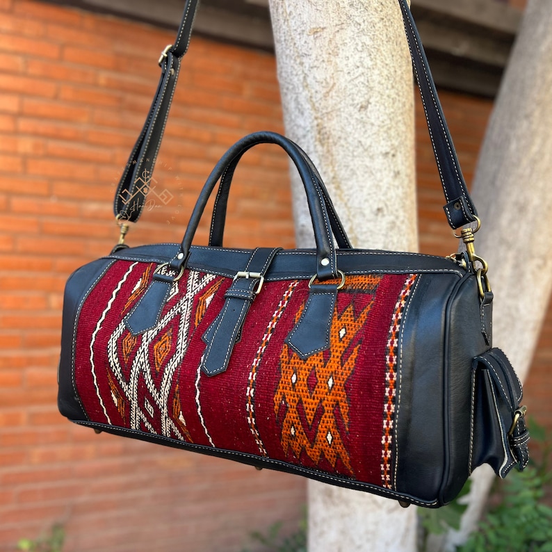 May include: A black leather duffel bag with a red, orange, and white woven pattern. The bag has a top handle and a shoulder strap.