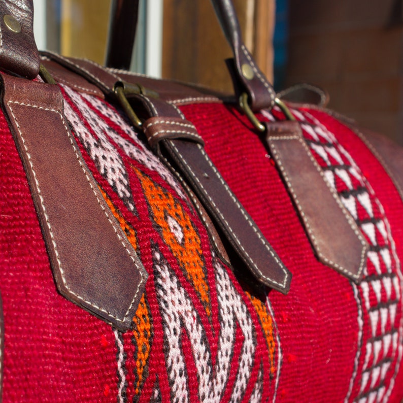 May include: A red and white patterned duffel bag with brown leather straps and buckles.