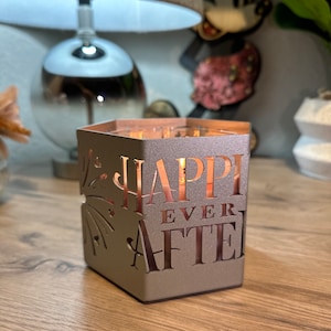 May include: A gray candle holder with a cut-out design of fireworks and the words "Happy Ever After".